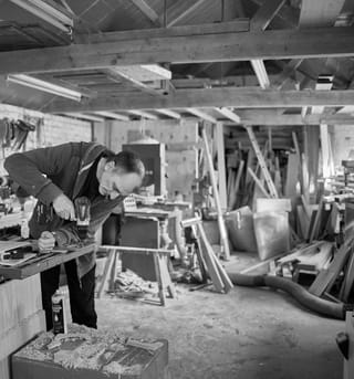 Alastair bent over the bench with a drill in his Westwood workshop, timber stacked behind him and sawdust on the floor.